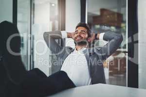 When you invest in yourself and it pays off. Shot of a handsome young businessman relaxing with his feet up on a desk in a modern office.