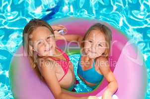 Summer rocks. Two little girls using an inflatable tube while swimming.