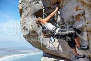 Adrenaline is pushing her to the summit. A young woman climbing up a rock face while framed against a blue sky.