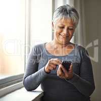 Connect to happiness. Shot of a mature woman stadning by a window on a sunny day.