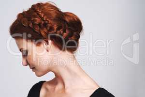 Soft and romantic. Studio shot of a beautiful redhead woman with a braided up-do posing against a gray background.