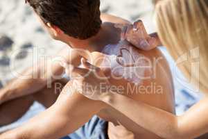 She shows her love where ever she can. A young woman making a heart shape with sunscreen on her boyfriends back.