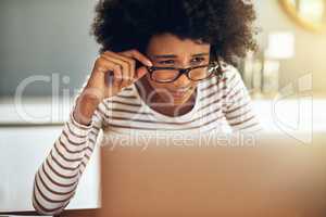 Am I reading this correctly. Shot of a focused young woman working on her laptop while holding her reading glasses at home during the day.