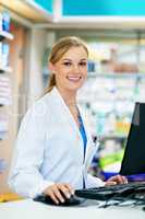 Let me bring up your details on the computer. Shot of a young pharmacist using a computer at the checkout counter.