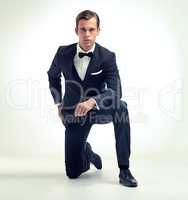 A gentlemans attire. A studio portrait of a handsome young man in a vintage pinstripe suit kneeling.