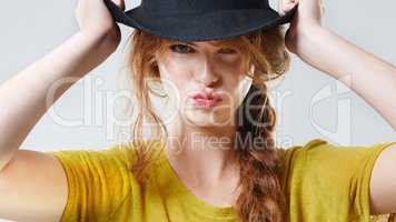 Why fit in when you were born to stand out. Closeup studio portrait of a beautiful young woman pouting while wearing a black hat.