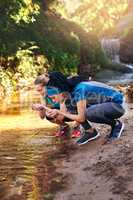 Everything you need is in nature. Shot of two sporty young women drinking water from a water stream.