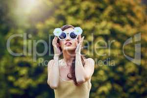 The sun loves her. Portrait of an attractive young woman wearing sunglasses while holding them and standing outside in nature during the day.