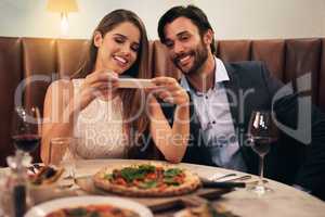I want to remember this pizza. Shot of a happy young couple taking a picture of their meal on a cellphone during a romantic dinner date at a restaurant.