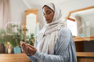 Prayer should not be regarded as a duty. Shot of a young muslim woman praying in the lounge at home.