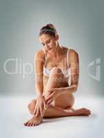 Staying silky soft. Studio shot of a young woman in underwear caressing her legs against a gray backgroundt.