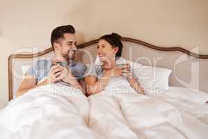 Starting off our morning on a warm note. Shot of a happy young couple drinking coffee in bed in their bedroom at home.