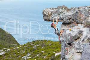 Maintaining a strong grip. A young woman rock climbing up the side of a mountain.