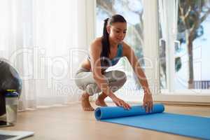 Boost your wellbeing by exercising regularly. Shot of a young woman rolling a yoga mat at home.