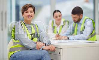 Weve got big plans. Cropped portrait of an attractive young female construction worker sitting in the boardroom with her colleagues in the background.