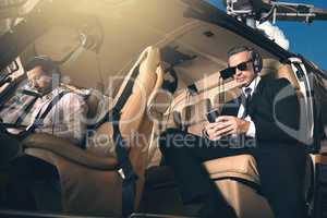 Premium business requires premium transport. Shot of a mature businessman using a mobile phone while traveling in a helicopter.