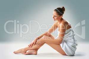 Luxuriously soft. Studio shot of a young woman in a towel caressing her legs against a gray background.