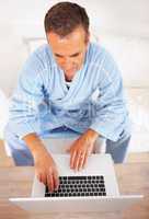 An elderly man in bathrobe working on a laptop at home. Upward view of a senior retired man working on a laptop at home.