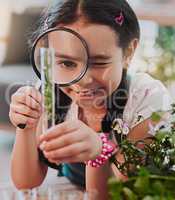 Looking at the bigger picture. Cropped shot of an adorable little girl looking through a magnifying glass while analysing plants from a test tube at home.