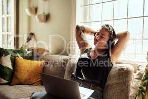 Good music washes the worries of the week away. Shot of a young woman using a laptop and headphones on the sofa at home.