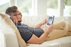 Need to unwind Theres an app for that. Shot of a handsome mature man relaxing on the sofa at home.