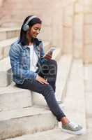 My network allows me to enjoy buffer-free entertainment. Shot of a young woman wearing headphones while using her cellphone out in the city.