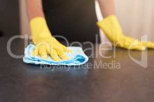 Spotless and germ free. Cropped shot of a person wearing rubber gloves while wiping a kitchen table with a cloth at home.