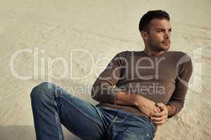 Looking stylish in the desert. A handsome male model reclining on the desert sand in trendy clothing.