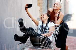 Their friendship brings them all the peace in the world. Cropped shot of two cheerful young girlfriends taking a selfie while playing around with a shopping cart outdoors.