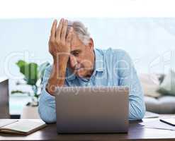 Oh no, not again. Shot of a mature man sitting alone and feeling stressed while using his laptop to work from home.