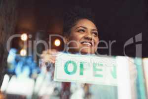 Customers will soon come flooding in. Cropped shot of a young woman hanging up an open sign on the window of her cafe.