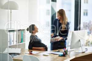 This office is positively glowing. Shot of a pregnant businesswoman and a colleague using a digital tablet together in an office.