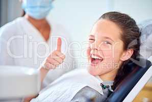 In the hot seat. Portrait of a young girl sitting in a dentists chair giving a thumbs up.