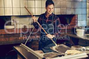 Master pizza maker at work. Shot of a young man using a peel while making a pizza behind the counter of a pizzeria.