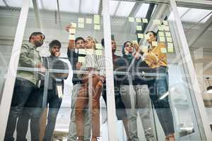 Working through their best concepts. Shot of a group of businesspeople brainstorming with notes on a glass wall in an office.