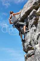 Adrenaline is pushing her to the summit. A young woman climbing up a rock face while framed against a blue sky.