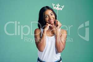The cutest queen ever. Studio portrait of a beautiful young woman posing with a prop crown against a green background.
