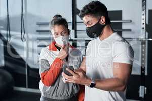 The stats will continue to rise if we dont stay safe. Shot of two sporty people looking at something on a cellphone together in a gym.