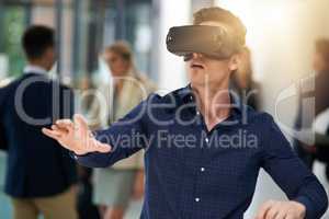 Immersed in a virtual world. Shot of a young businessman wearing a VR headset in a busy office.