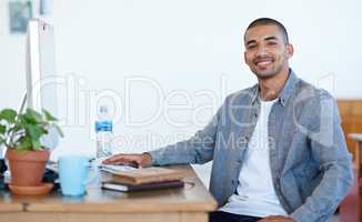 Portrait of a handsome young man working at his computer in an office. The commercial designs displayed in this image represent a simulation of a real product and have been changed or altered enough by our team of retouching and design specialists so that