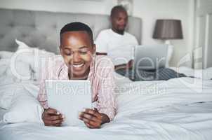 Turning on the day with their favourite devices. Shot of a happy young woman using a digital tablet while her husband uses a laptop in bed at home.