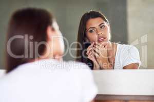 Where did that come from. Shot of a frowning young woman examining an imperfection on her skin in the mirror at home.