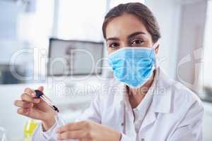 Time for some testing. Portrait of a confident young female scientist wearing a surgical mask while doing a experiment and looking at the camera inside a laboratory.