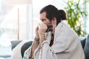 This is the worst time to be sick. Shot of a sickly young man blowing his nose with a tissue in his living room.