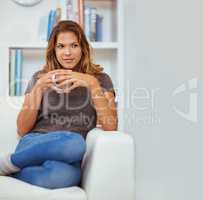 Timeout with some tea. Portrait of a young woman enjoying a warm beverage at home.