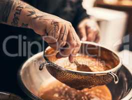 This dish is a knock out. Closeup of a unrecognisable chefs tattooed hands straining food into a bowl in kitchen of a restaurant.