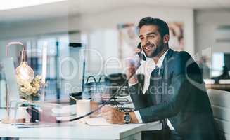 He is always ready to receive business calls. Shot of a cheerful young businessman making a call while being seated inside of the office.