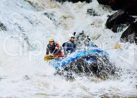 We asked for extreme adventure and we got it. Shot of a group of determined young men on a rubber boat busy paddling on strong river rapids outside during the day.