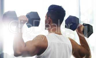 Its a commitment he makes every day. Rearview shot of a handsome young sportsman working out with dumbbells in a gym.