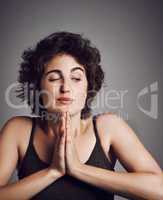 Still a bit scared of the dark. Studio shot of an attractive young woman with her hands in prayer position against a grey background.